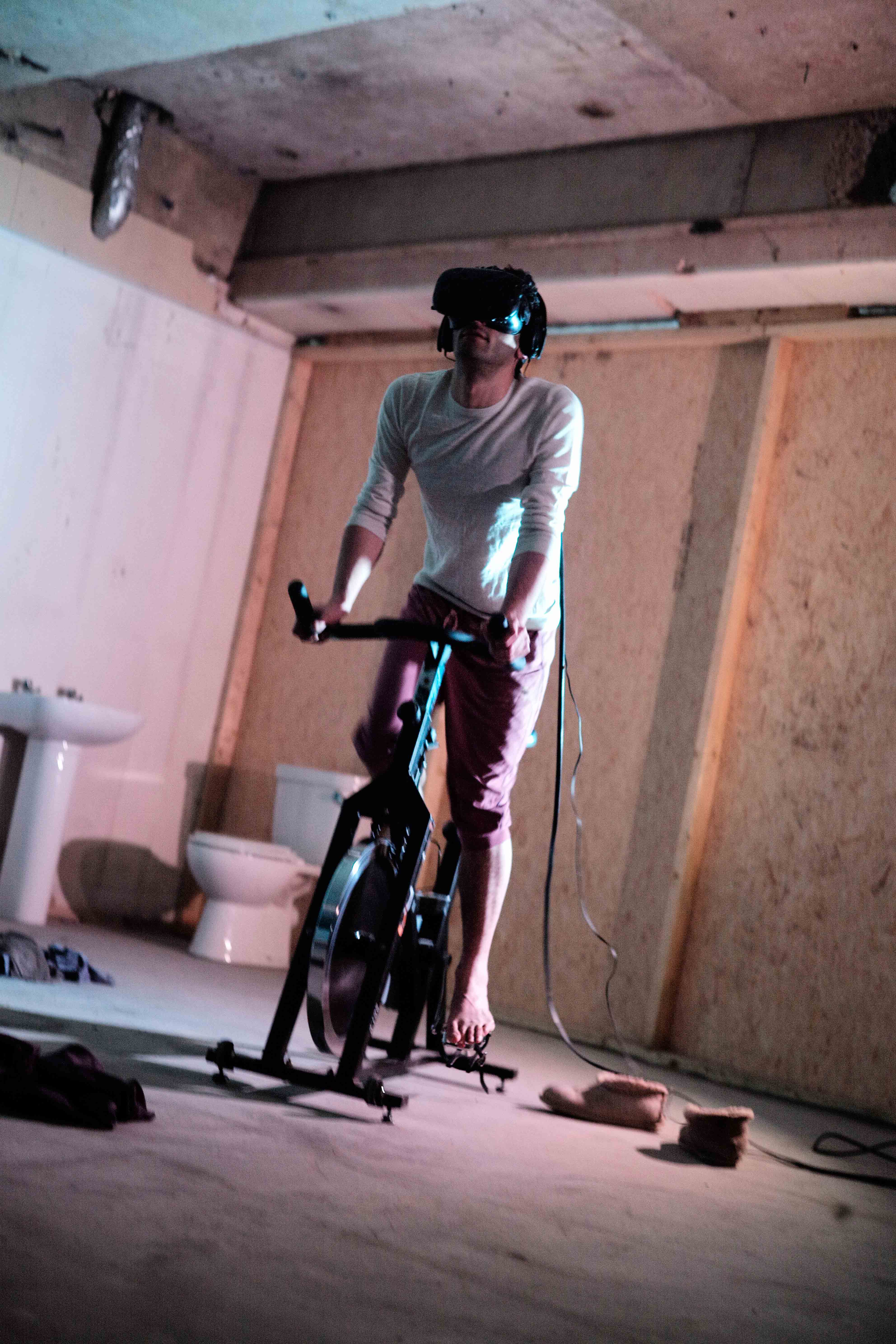 An action shot of the artist wearing the VR headset whilst using the exercise bike.
