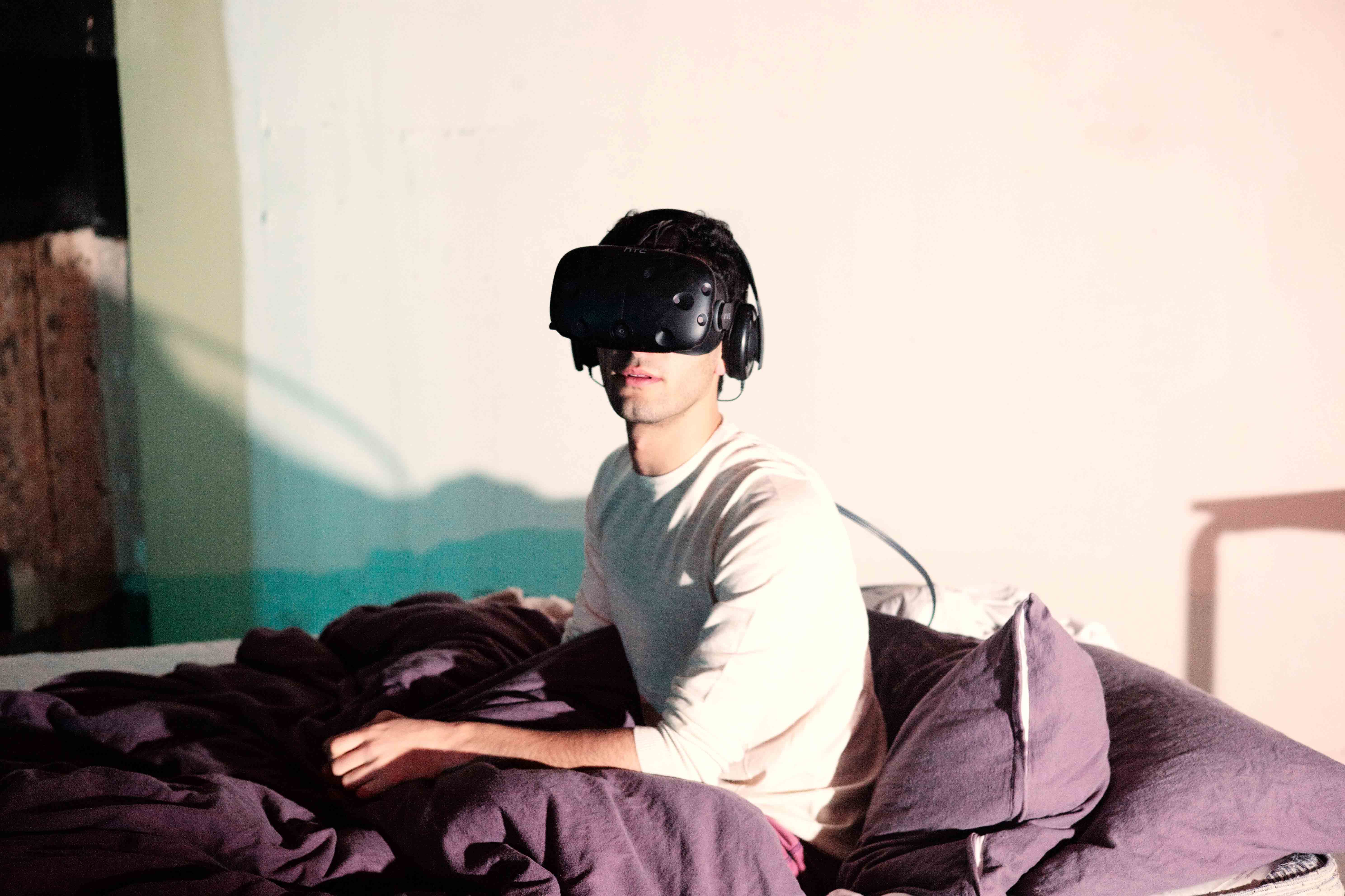 The artist wearing the VR headset, in bed.