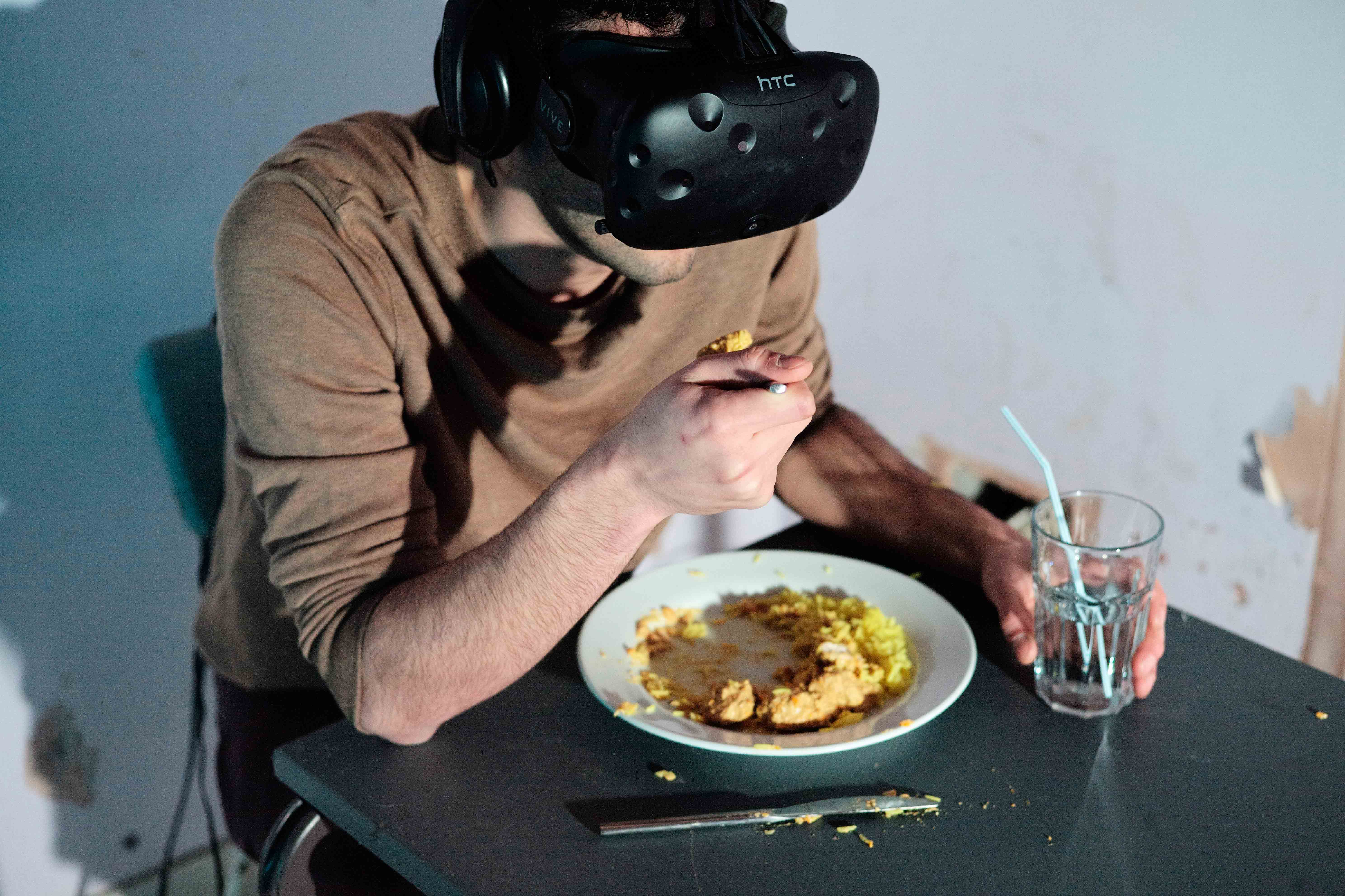 The artist wearing the VR headset eating a curry at the table.