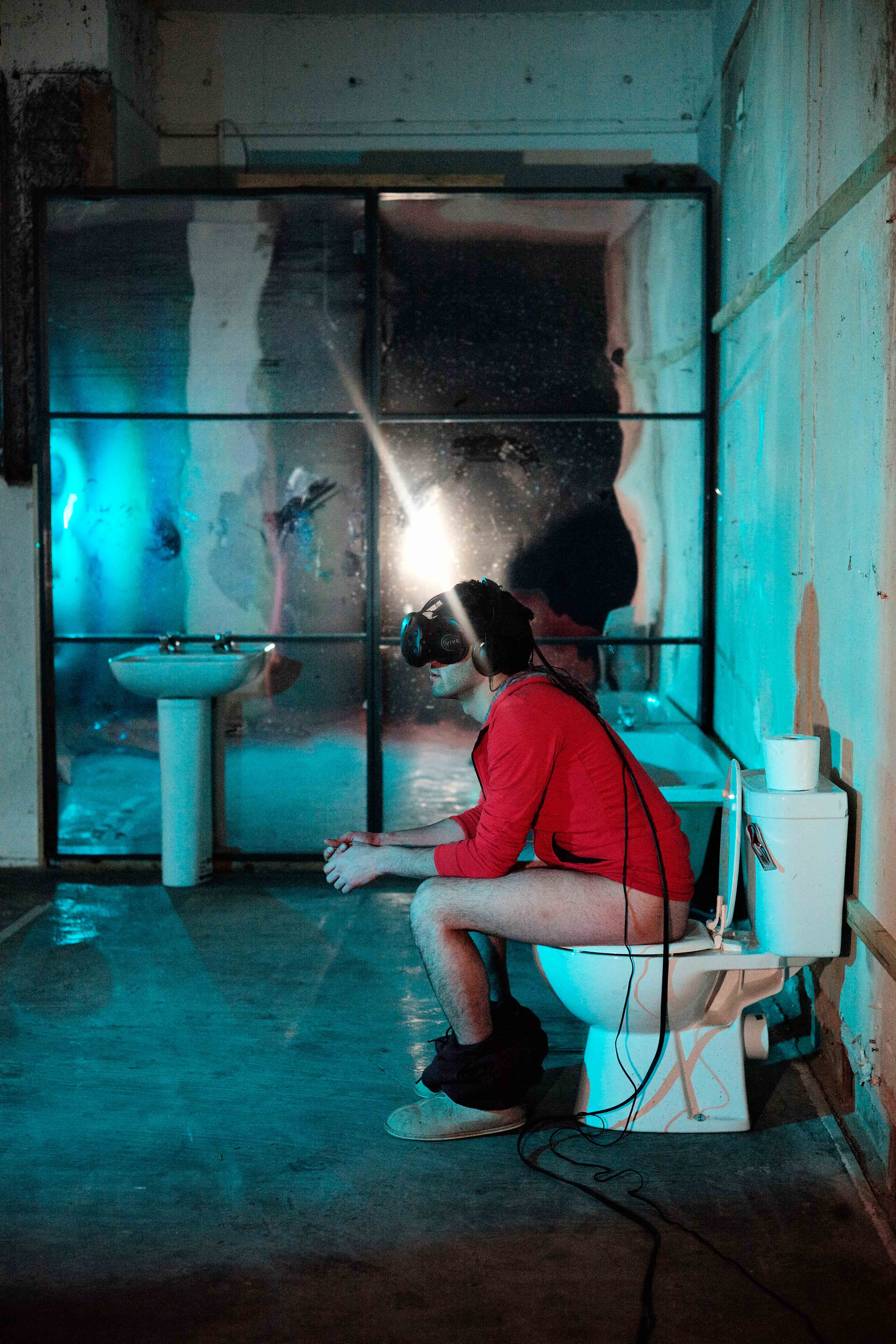 A side view of the artist wearing the VR headset whilst using the toilet.